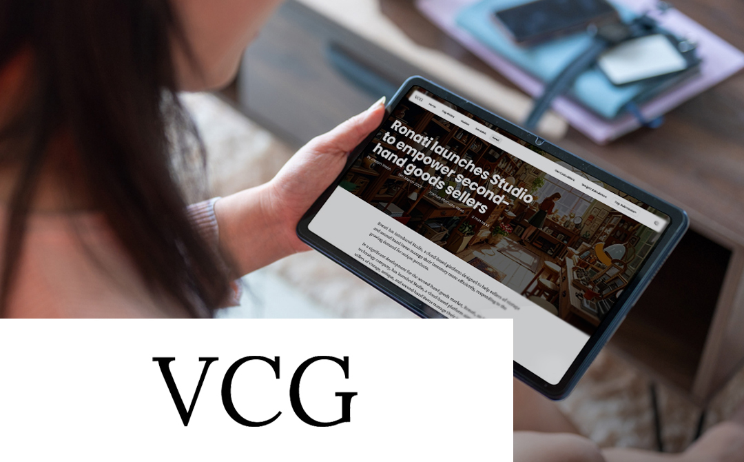 A person holding a tablet displaying the Ronati website with the headline 'Ronati launches Studio to empower second-hand goods sellers' visible on screen. The tablet shows text about Ronati's new platform for vintage and antique sellers. In the background, there are papers or notebooks on a table. At the bottom of the image, 'VCG' (Vintage Clothing Guides) is displayed in large black text against a white background. The image illustrates the March 2025 announcement of Ronati's new cloud-based inventory management platform for the second-hand market.