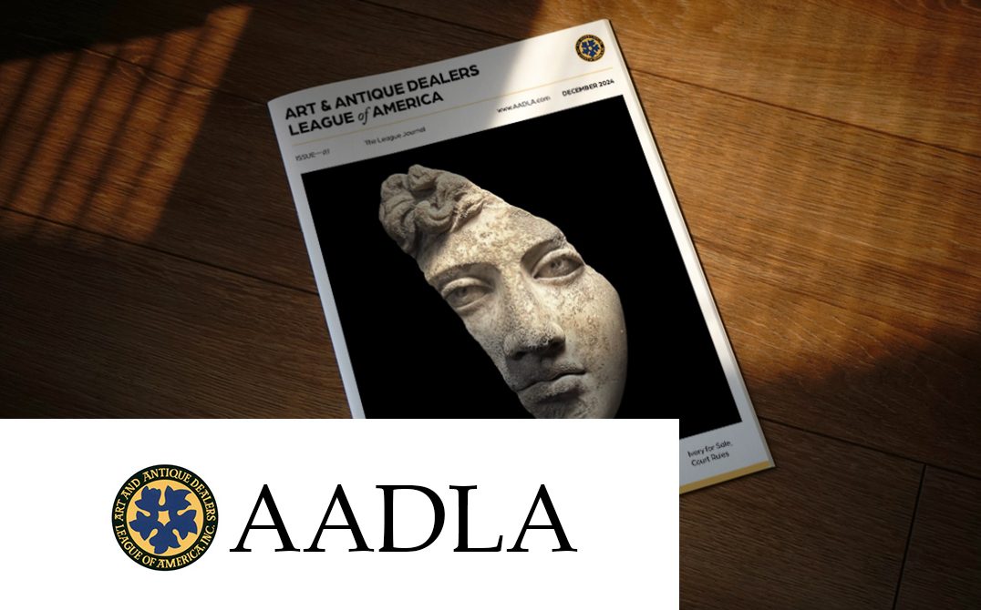 The cover of the Art & Antique Dealers League of America (AADLA) journal from December 2024, featuring a classical marble sculpture fragment of a face against a black background. The magazine rests on a wooden surface, with dramatic lighting highlighting its white cover. At the bottom of the image is the AADLA logo, featuring a circular blue emblem with gold accents alongside the text 'AADLA' in large black letters.