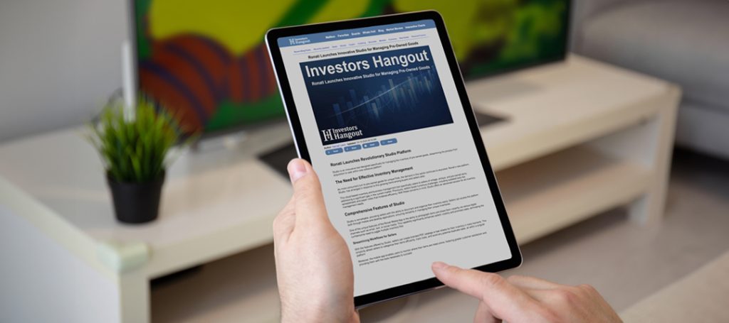 A close-up image of hands holding a tablet displaying an article from 'Investors Hangout' about Ronati. The tablet screen shows a headline reading 'Investors Hangout: Ronati Launches Innovative Studio for Managing Pre-Owned Goods' with article text visible below including sections titled 'Ronati Launches Revolutionary Studio Platform' and 'The Need for Effective Inventory Management' followed by 'Comprehensive Features of Studio'. One hand is holding the tablet while another finger is touching the screen. In the background is a minimalist white furniture piece with a small potted plant, and colorful artwork with yellow and red elements can be seen on the wall.