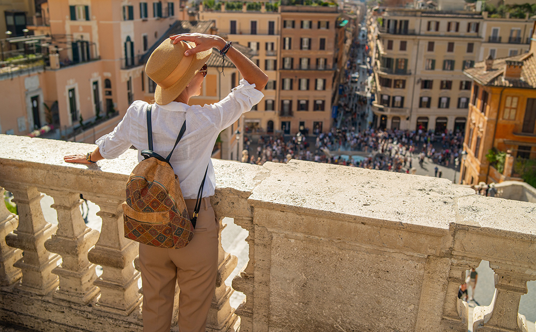 Tourist with straw hat overlooking crowded Italian piazza from ornate stone balcony, representing increased cultural tourism and collector interest following Italy's VAT reduction on art and antiques