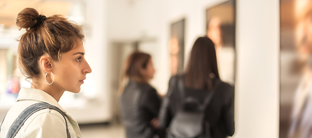 Young woman viewing artwork in contemporary gallery setting, representing the increased buyer confidence and accessibility that Italy's reduced VAT rate brings to art collectors and interior designers