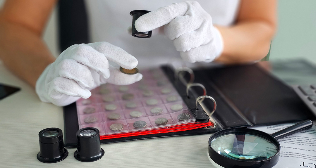 Professional appraiser examining vintage coins with magnifying glass, highlighting the expertise and authentication crucial to the antiques trade