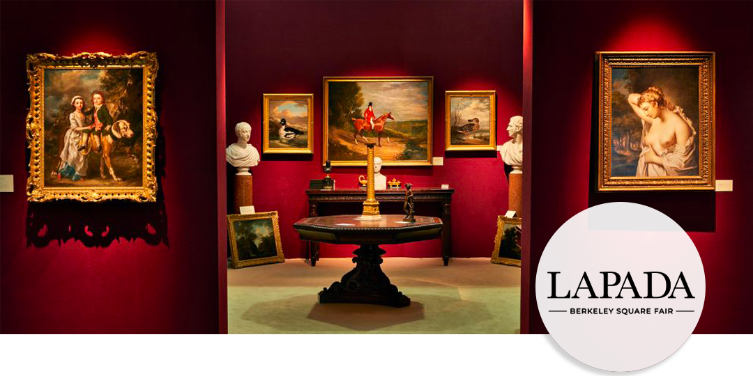 Exhibition booth at LAPADA Berkeley Square Fair with Old Master paintings, marble busts, and period furniture against deep red walls.