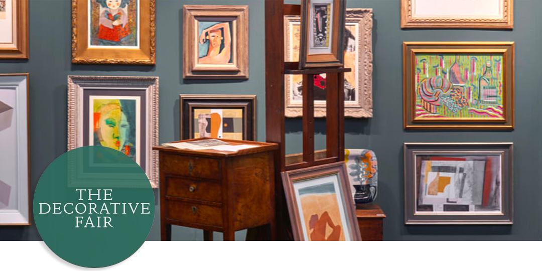 Eclectic display at The Decorative Fair featuring mid-century and modern artworks, framed prints, and vintage furniture pieces.