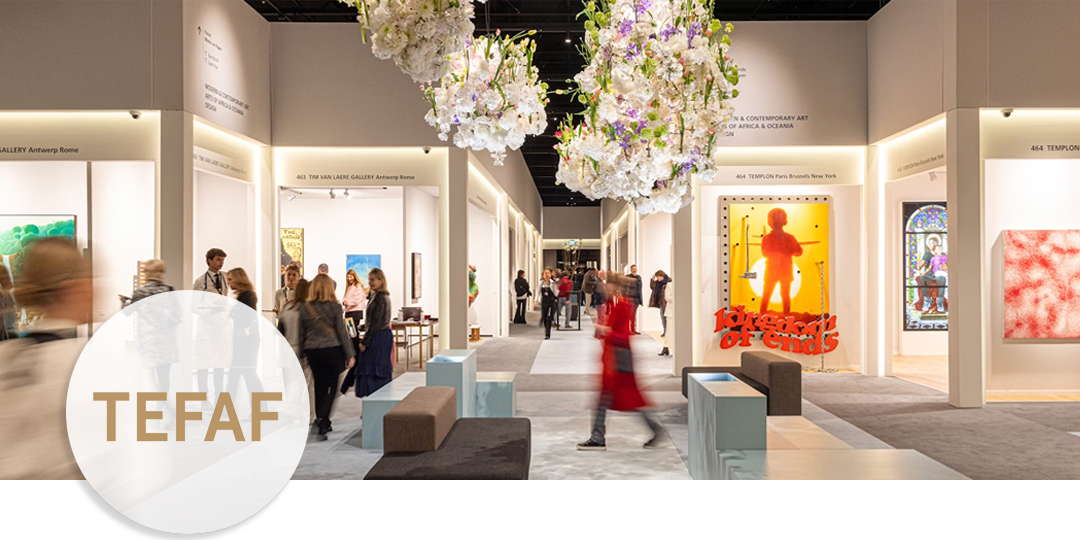 TEFAF Maastricht fair entrance hall with flower installation overhead and visitors browsing museum-style booths.