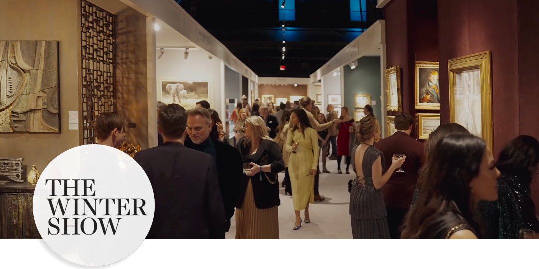 Elegant crowd mingling in the Park Avenue Armory’s historic hall during The Winter Show, surrounded by fine art and antiques in warmly lit booths.