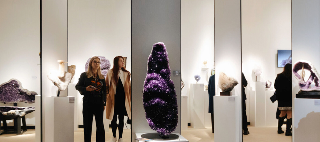 Visitors admiring large amethyst geodes and mineral specimens at a contemporary jewelry and gemstone exhibit within the LAPADA Fair.